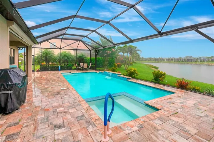 View of pool with glass enclosure, a sunroom, area for grilling, a patio area, and a water view