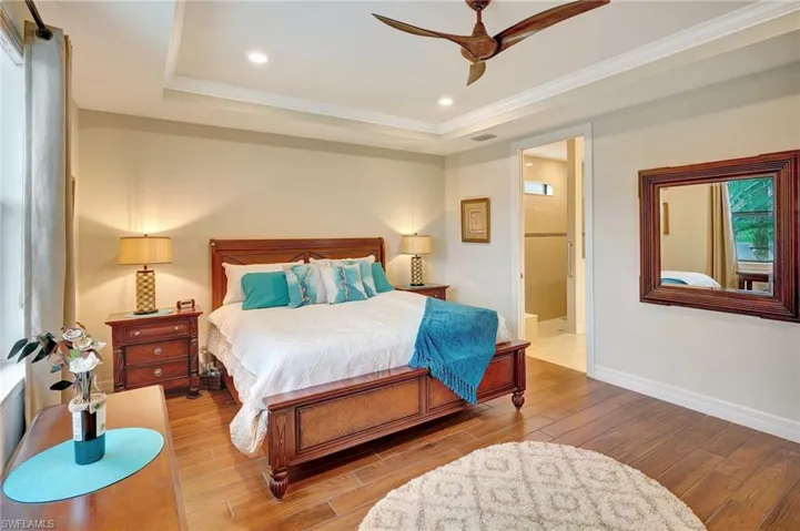 Bedroom with wood finished floors, a tray ceiling, ensuite bathroom, recessed lighting, and ornamental molding