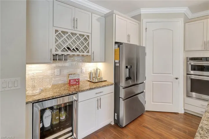 Kitchen featuring appliances with stainless steel finishes, beverage cooler, light stone countertops, dark wood-style flooring, and crown molding