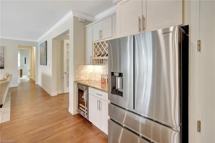 Kitchen with stainless steel fridge with ice dispenser, ornamental molding, white cabinets, light stone countertops, and light wood finished floors