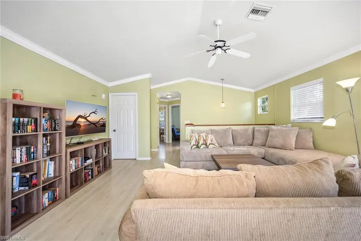 Living room with ornamental molding, lofted ceiling, light wood finished floors, and ceiling fan