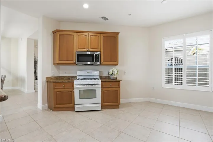 Kitchen featuring gas range gas stove, stainless steel microwave, wood finish cabinets, dark stone counters, and light tile patterned floors