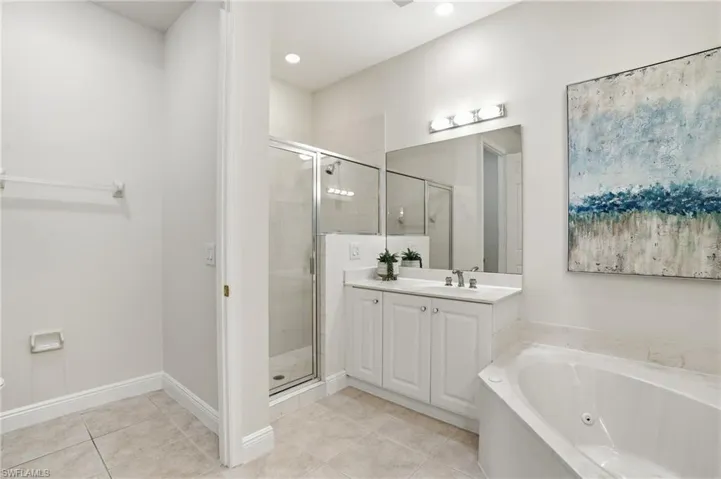 Primary bathroom with a shower stall, vanity, a whirlpool tub, and light tile patterned flooring