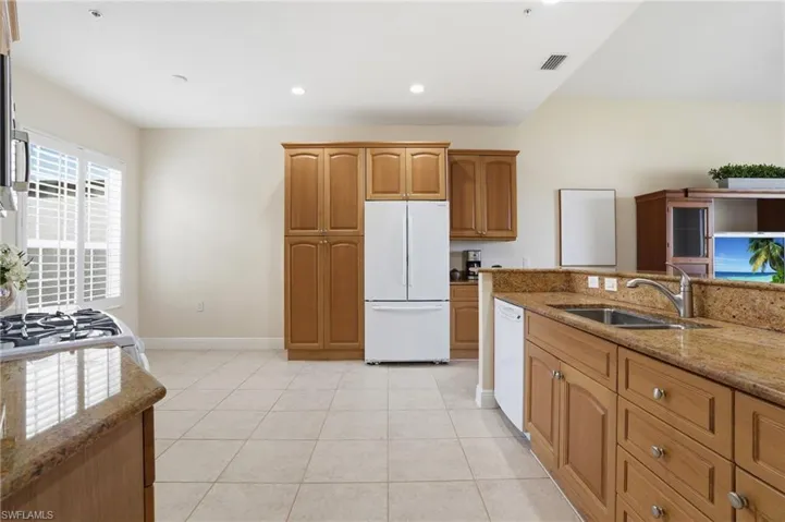 Kitchen featuring light stone counters, white appliances, wood finish cabinetry, light tile patterned floors, and recessed lighting