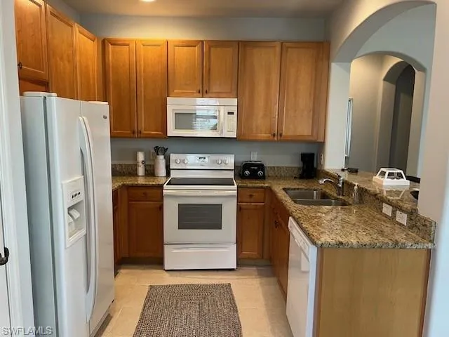 Kitchen with dark stone counters, white appliances, brown cabinets, and light tile  floors