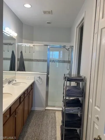 Bathroom featuring double vanity, a shower stall, light tile patterned floors, and recessed lighting