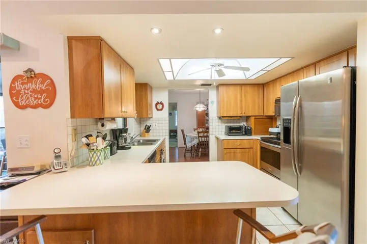 Kitchen with breakfast bar, stainless steel appliances, a peninsula, light countertops, decorative backsplash, and recessed lighting