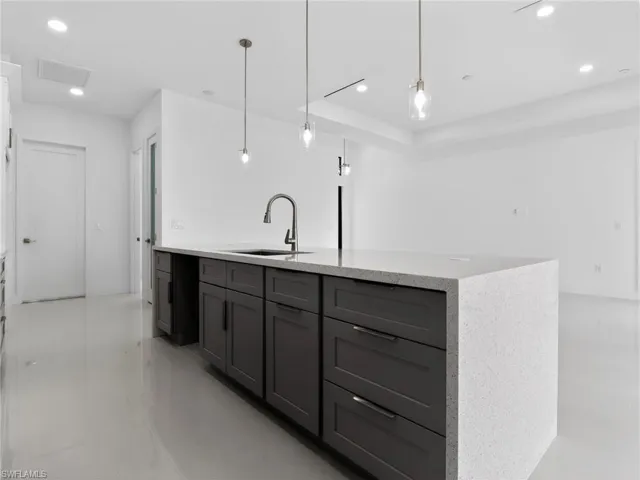 Spacious kitchen featuring a large island with dark cabinetry, a built-in sink with a modern faucet, and light-colored countertops