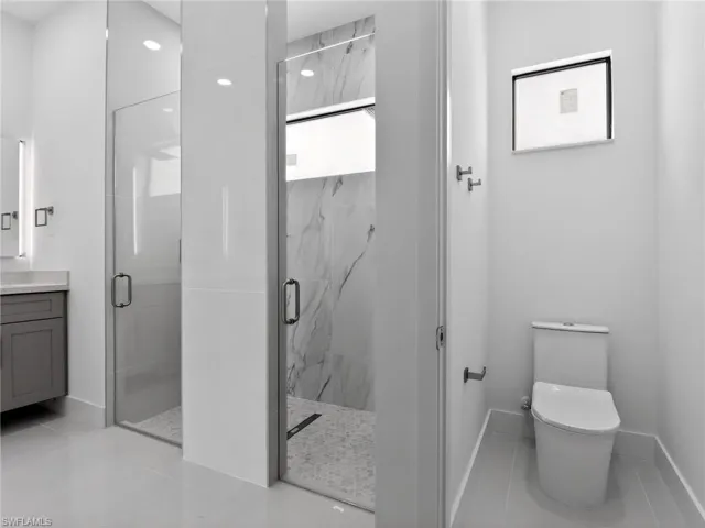 Bathroom featuring dual glass-enclosed showers, a vanity with a grey cabinet and a light-colored countertop, and a white toilet