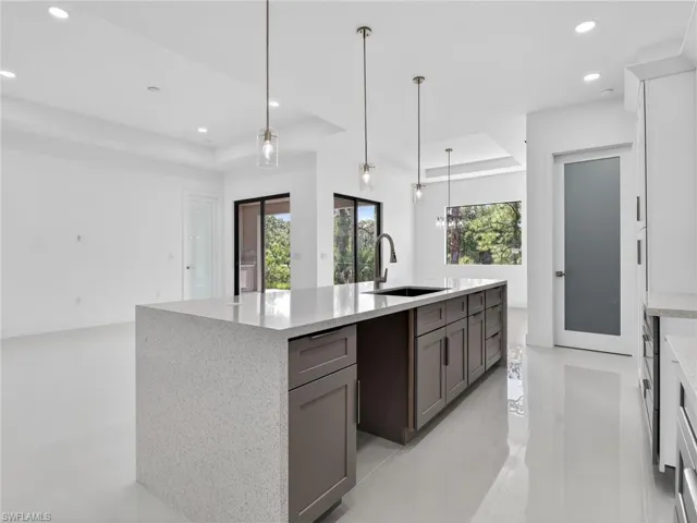 The kitchen features a large island with a light-colored countertop and dark cabinetry, pendant lighting, and a modern sink with a high-arc faucet
