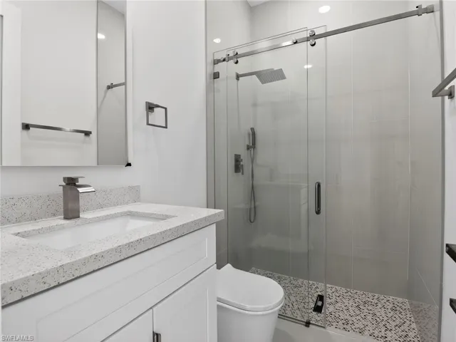 This bathroom features a contemporary vanity with a speckled countertop, a modern faucet, and a spacious shower with a glass enclosure and rain shower head