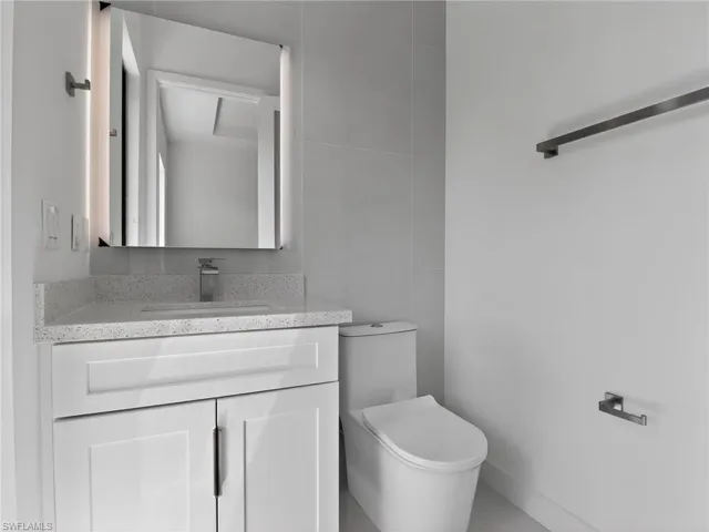 Modern bathroom vanity with a light speckled countertop, an integrated sink, and an illuminated mirror