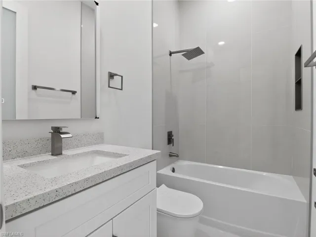 Bathroom featuring a vanity with a white countertop and an integrated sink, a rectangular mirror, a bathtub with a rainfall showerhead, and white tiled walls