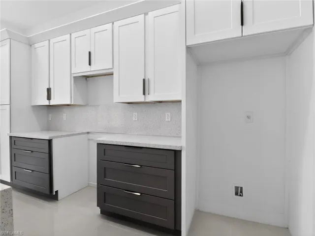Kitchen featuring white upper cabinetry, dark lower cabinetry, light-colored countertops, and a matching backsplash