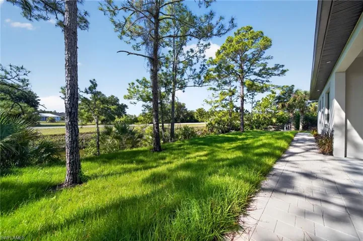 Exterior paver pathway alongside a green lawn and mature pine trees