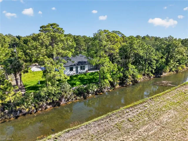Waterfront property featuring a single-story residence with a dark shingle roof, white siding, and dark-framed windows