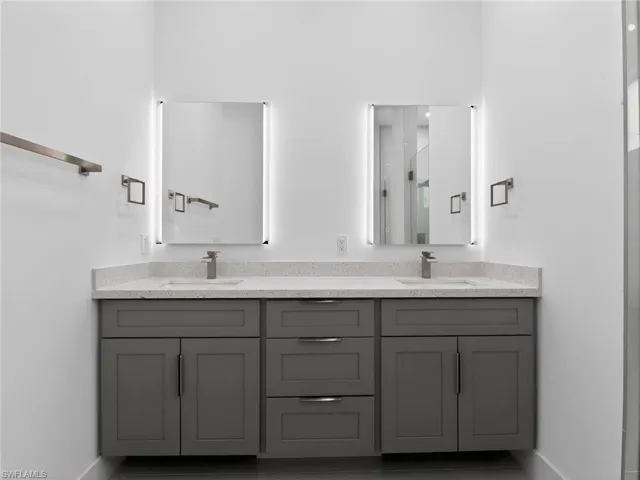 Bathroom featuring a double vanity with grey cabinetry, a light-colored speckled countertop, and two rectangular mirrors with integrated lighting