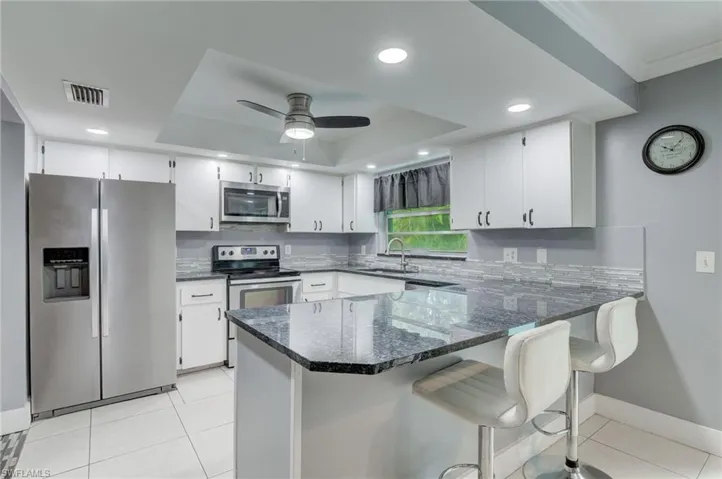 Kitchen featuring stainless steel appliances, a tray ceiling, and light tile floors