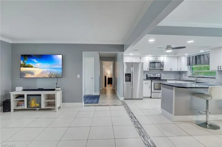 Kitchen featuring ceiling fan, kitchen peninsula, light tile floors, white cabinets, and appliances with stainless steel finishes