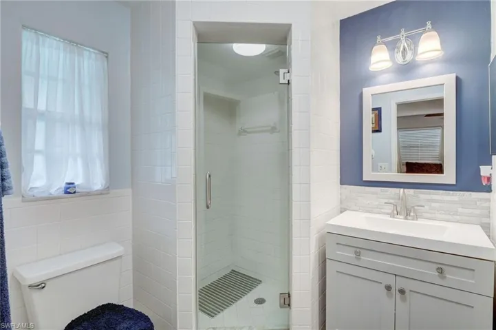 Bathroom featuring a shower with door, vanity, toilet, and tile walls