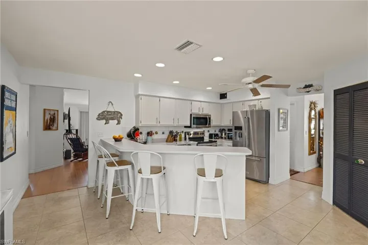Kitchen with light tile patterned flooring, white cabinetry, ceiling fan, appliances with stainless steel finishes, and kitchen peninsula