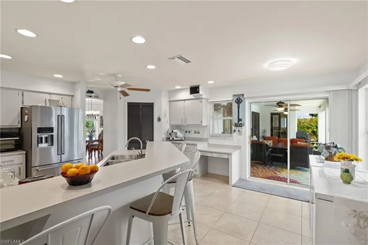 Kitchen featuring ceiling fan, stainless steel fridge with ice dispenser, sink, light tile patterned floors, and backsplash