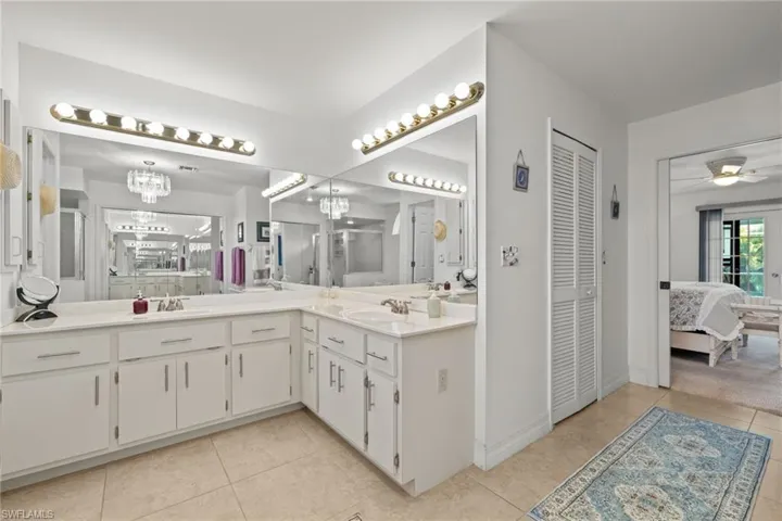Bathroom with tile patterned floors, ceiling fan with notable chandelier, and dual bowl vanity