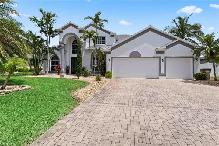 A stately two-story colonial home set against a lush tropical backdrop, featuring a freshly painted exterior, new roof, and a spacious three-bay garage.