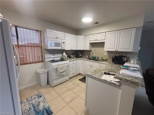 Kitchen with white appliances, a peninsula, white cabinetry, light tile patterned flooring, and backsplash