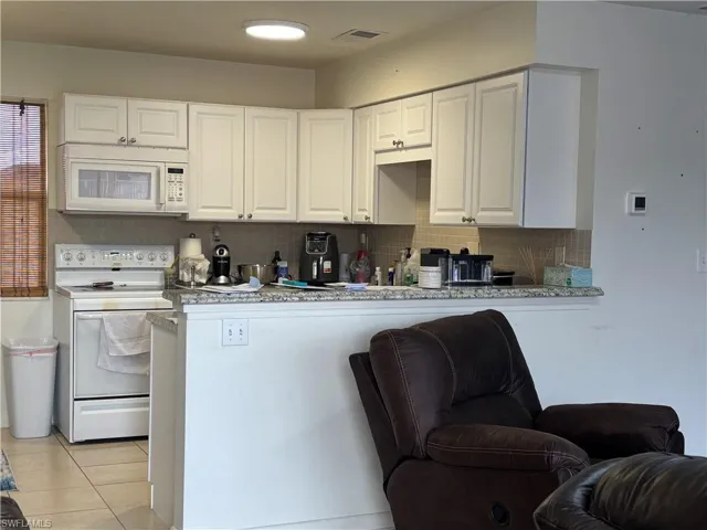 Kitchen with white appliances, decorative backsplash, and white cabinets