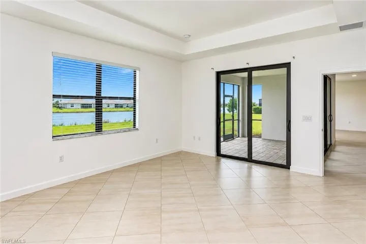 Neutral-toned tile flooring, recessed tray ceiling, large picture window, and sliding glass doors opening to a covered patio