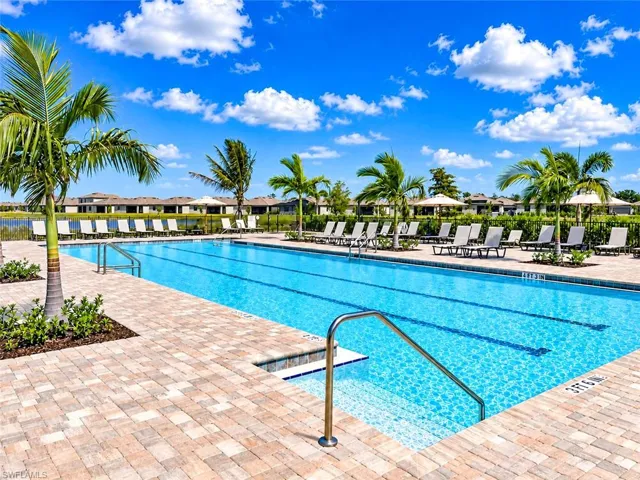 Lap pool featuring a paved deck, metal handrails, and tropical landscaping