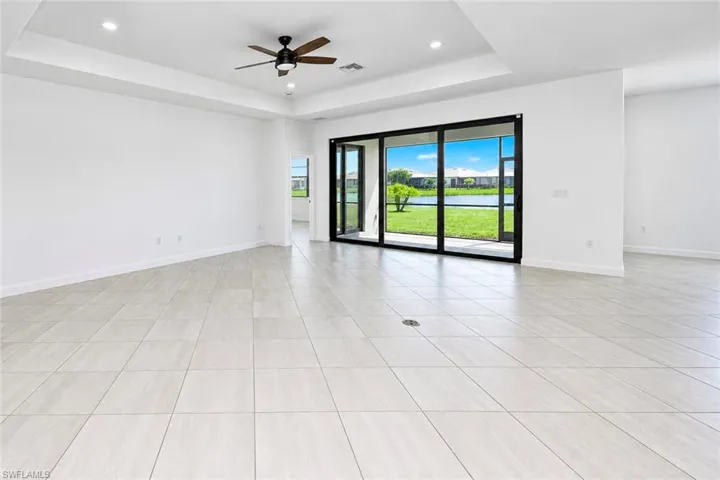 Open-concept space featuring large-format tile flooring, a tray ceiling, recessed lighting, a ceiling fan, and multi-panel sliding glass doors