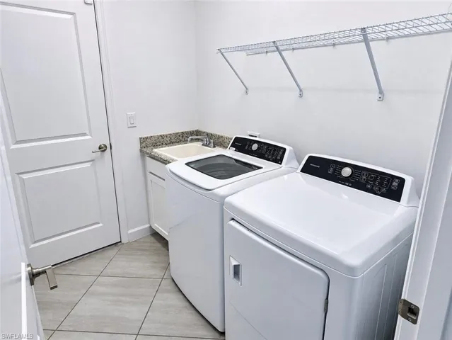 Laundry room featuring large-format ceramic tile flooring, stone-finish countertop, drop-in utility sink, white shaker-style cabinetry, and wall-mounted wire shelving