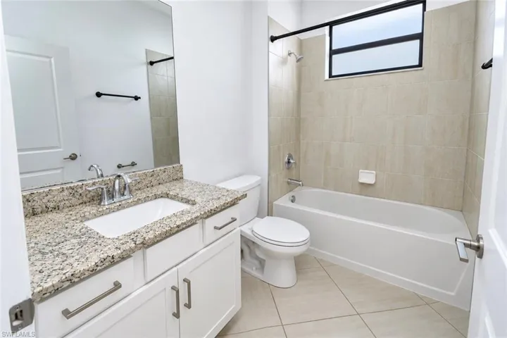 Bathroom featuring a vanity with stone-finish countertop, under-mount sink, white shaker-style cabinetry, and a bathtub-shower combination with tiled surround