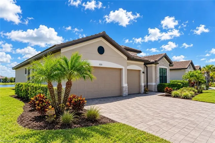 Single-story exterior featuring a stucco facade, stone accents, paver driveway, three-car garage, and manicured landscaping