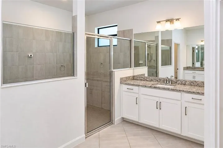 Bathroom featuring a vanity with stone-patterned countertop, white cabinetry, a glass-enclosed shower with tile surround, and a large-format mirror