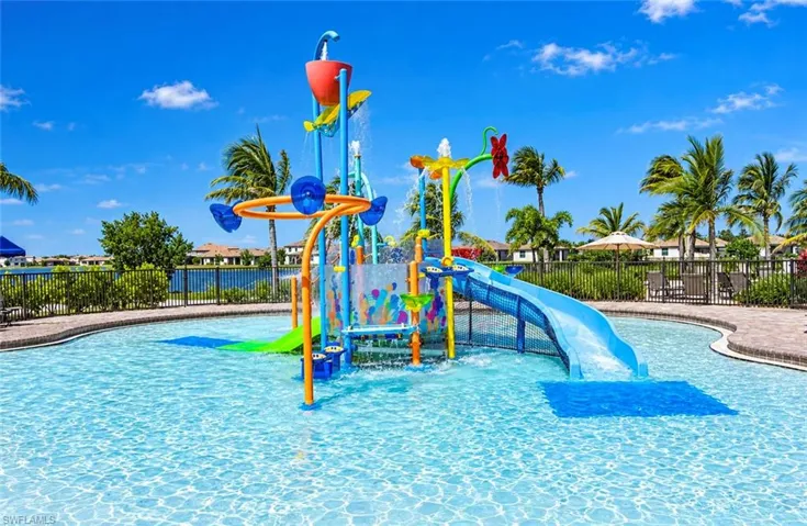 Aquatic recreation area featuring a water slide, multi-level spray structures, and a perimeter paved in stone pavers