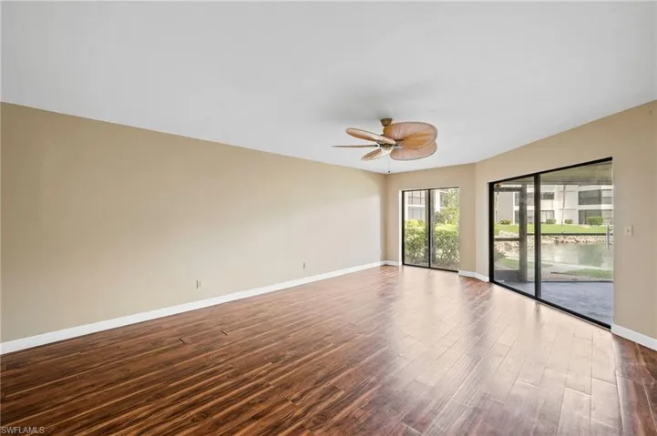 Empty room with dark wood-style flooring, a water view, and a ceiling fan