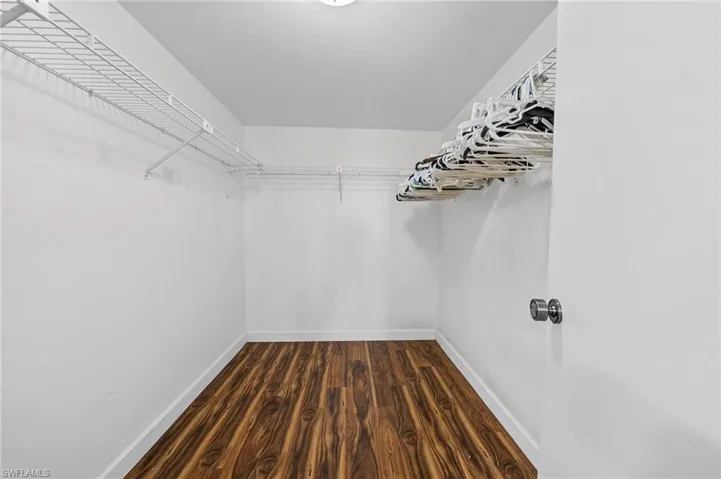 Walk in closet with dark wood-type flooring