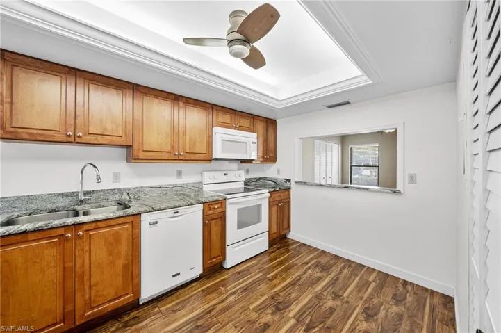 Kitchen with white appliances, light stone countertops, brown cabinetry, and dark wood-style floors