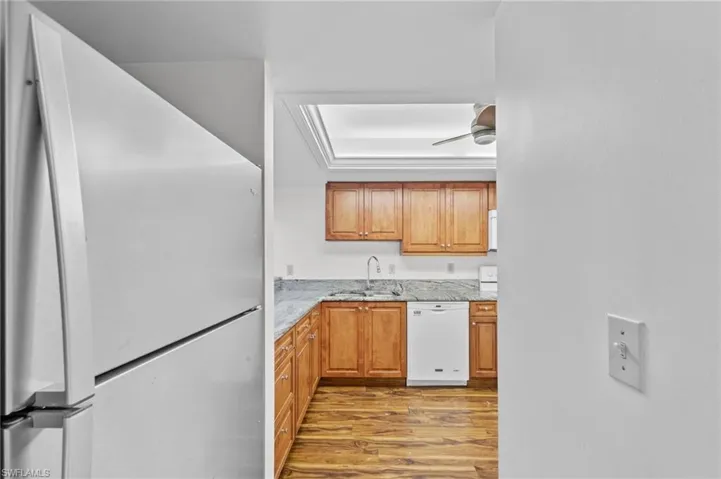 Kitchen featuring white appliances, dark wood finished floors, brown cabinets, and light stone countertops