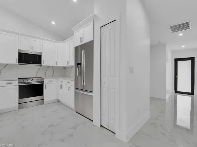 Kitchen featuring appliances with stainless steel finishes, light marble finish flooring, white cabinets, baseboards, and recessed lighting