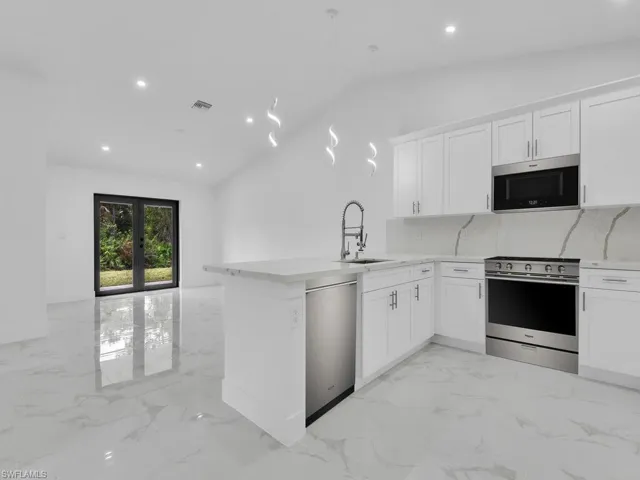 Kitchen with appliances with stainless steel finishes, a sink, vaulted ceiling, light marble finish flooring, and decorative backsplash