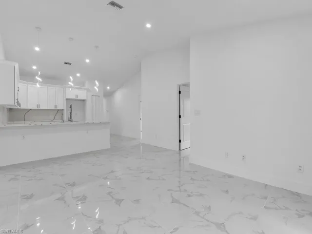 Unfurnished living room featuring vaulted ceiling, baseboards, light marble finish floors, recessed lighting, and a sink