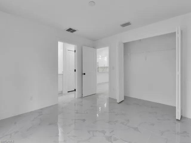Unfurnished bedroom featuring light marble finish floors, a closet, and ensuite bath