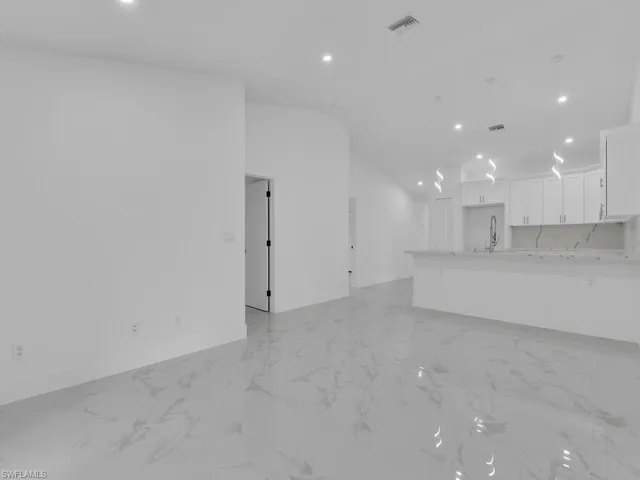 Unfurnished living room featuring light marble finish flooring, baseboards, a sink, lofted ceiling, and recessed lighting