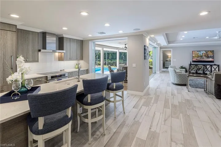 Kitchen featuring ceiling fan, light hardwood / wood-style floors, tasteful backsplash, a raised ceiling, and wall chimney exhaust hood