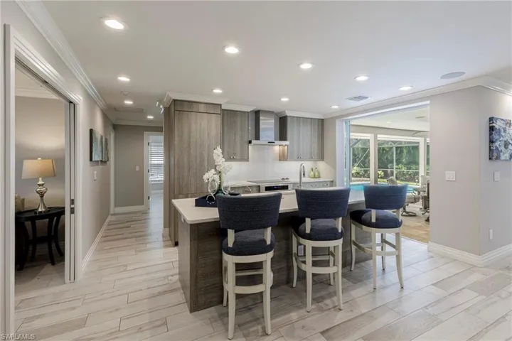 Kitchen with wall chimney range hood, tasteful backsplash, ornamental molding, light wood-type flooring, and a breakfast bar