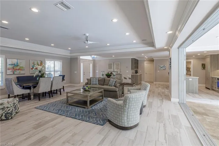 Living room with ceiling fan, a raised ceiling, crown molding, and light wood-type flooring